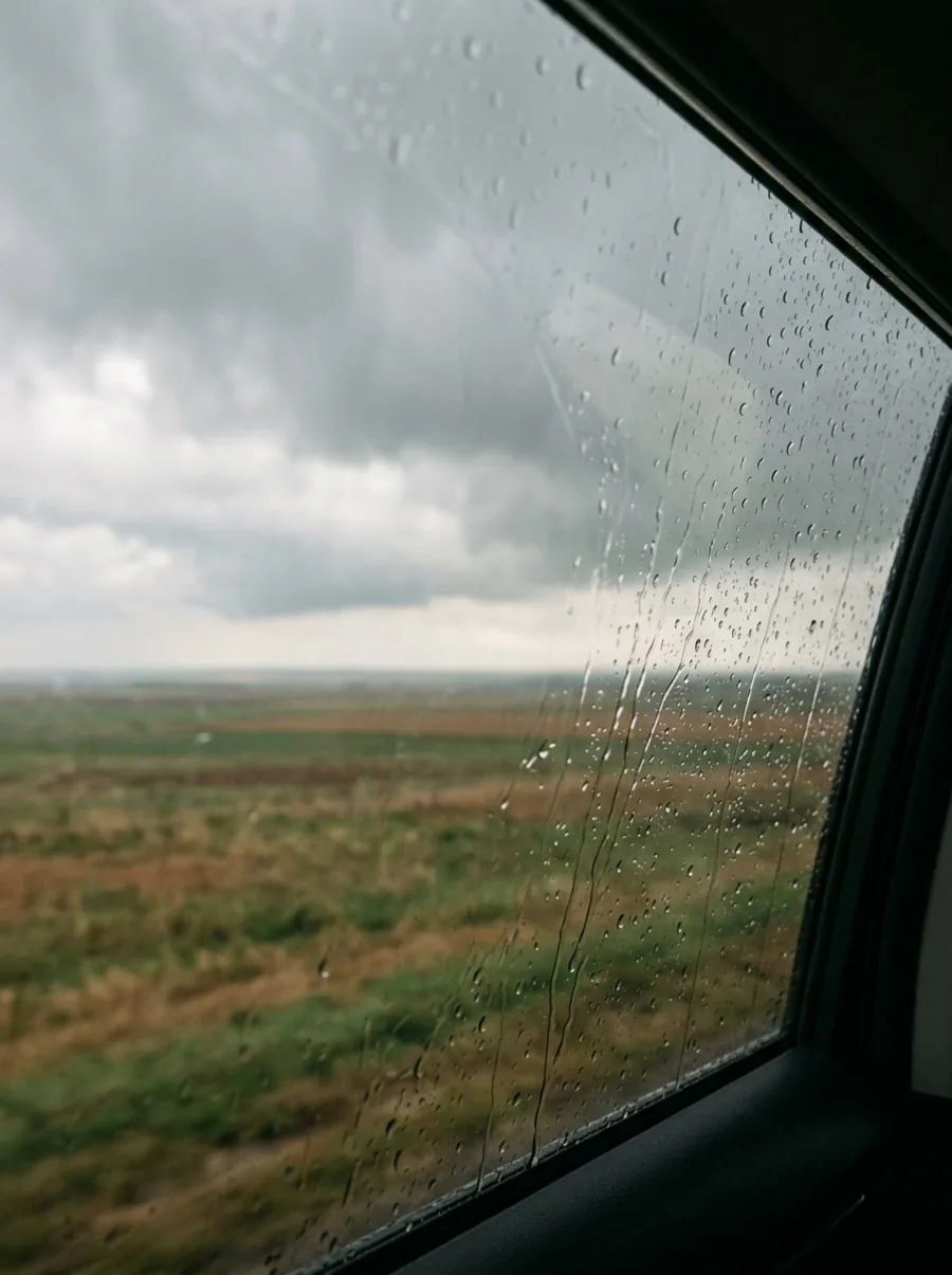 Rain on a car window looking out over an open plain under a heavy sky