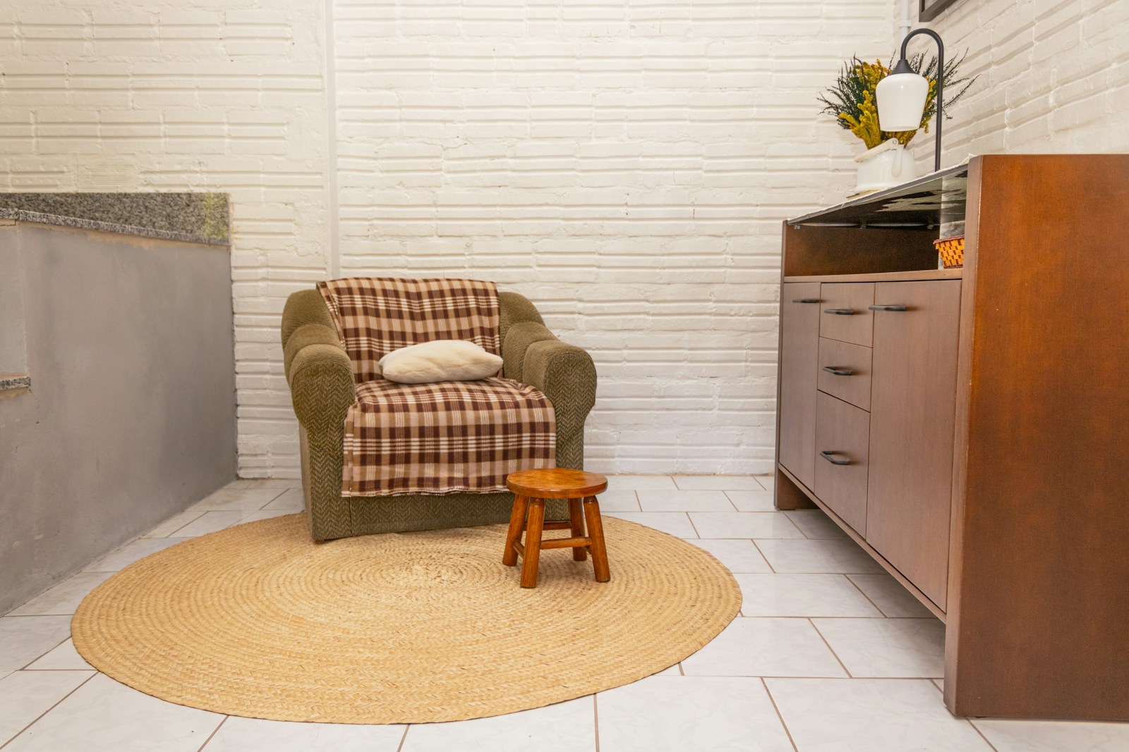 A linen armchair with a soft throw blanket in a quiet, naturally-lit corner — a steady place to do the work