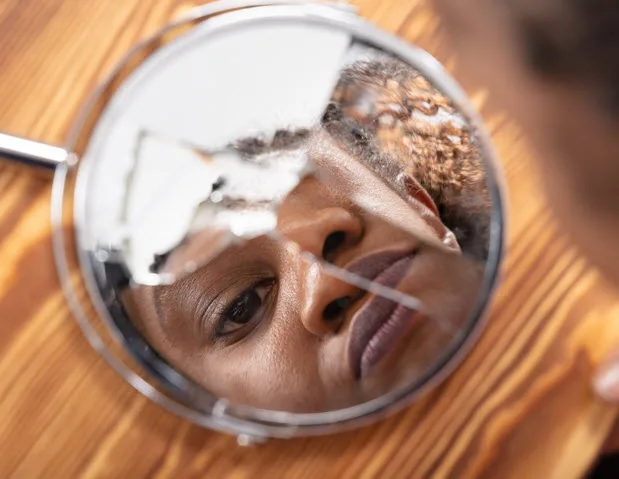 A woman's face reflected in a cracked hand mirror