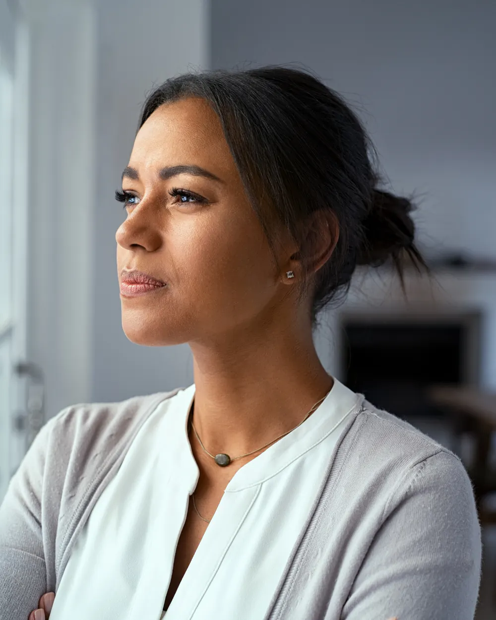 A woman standing near a window at home, looking into the distance